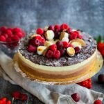 Delicious chocolate layered cake topped with fresh berries and meringue on a rustic backdrop.