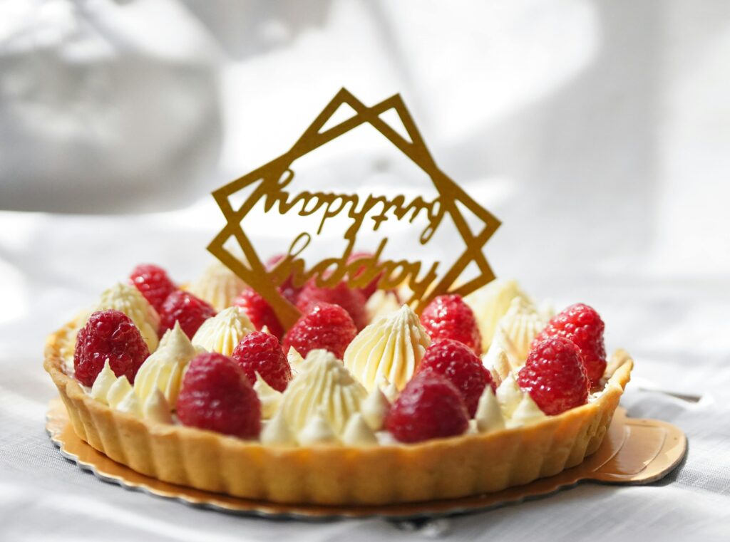 Delicious raspberry cream tart adorned with a 'Happy Birthday' topper, perfect for celebrations.