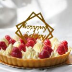 Delicious raspberry cream tart adorned with a 'Happy Birthday' topper, perfect for celebrations.